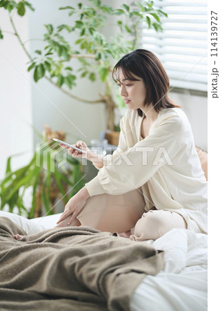 ベッドでスマートフォンを見る20代女性 ベッドでスマートフォンを見る20代女性 114139727