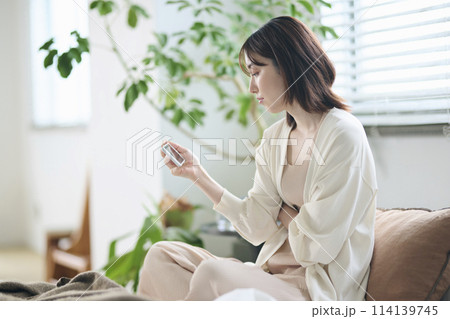 ベッドでスマートフォンを見る20代女性 ベッドでスマートフォンを見る20代女性 114139745
