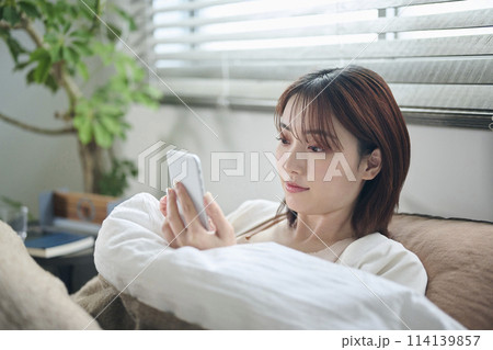 布団に入ってスマートフォンを見る20代女性 布団に入ってスマートフォンを見る20代女性 114139857