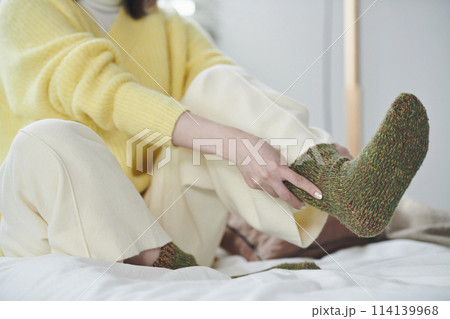ベッドの上で靴下を履こうとする20代女性の手元 ベッドの上で靴下を履こうとする20代女性の手元 114139968