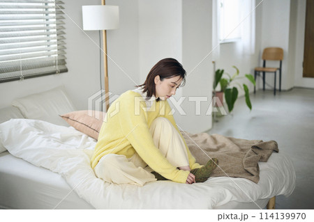 ベッドの上で靴下を履こうとする20代女性 114139970