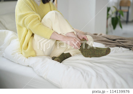 ベッドの上で靴下を履こうとする20代女性の手元 114139976
