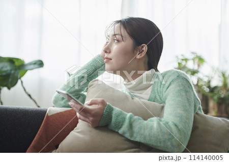 ソファでくつろぎながらスマートフォンを見る女性 114140005