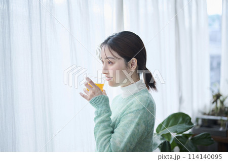 窓際でオレンジジュースを飲む20代女性 114140095