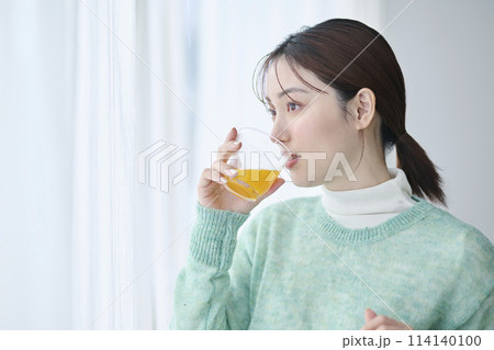 窓際でオレンジジュースを飲む20代女性 114140100