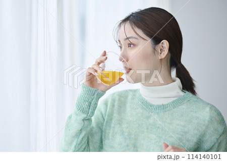 窓際でオレンジジュースを飲む20代女性 窓際でオレンジジュースを飲む20代女性 114140101