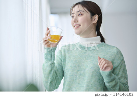 窓際でオレンジジュースを飲む20代女性 窓際でオレンジジュースを飲む20代女性 114140102