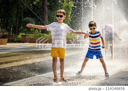 Boy having fun in water fountains. Child playing with a city fountain on hot summer day. Happy kids having fun in fountain. Summer weather. Active leisure, lifestyle and vacation Boy having fun in water fountains. Child playing with a city fountain on hot summer day. Happy kids having fun in fountain. Summer weather. Active leisure, lifestyle and vacation 114140656