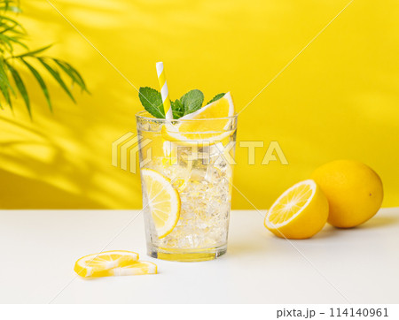 A glass of cold lemonade with lemon, mint and ice on a yellow and white background with a palm leaf A glass of cold lemonade with lemon, mint and ice on a yellow and white background with a palm leaf 114140961