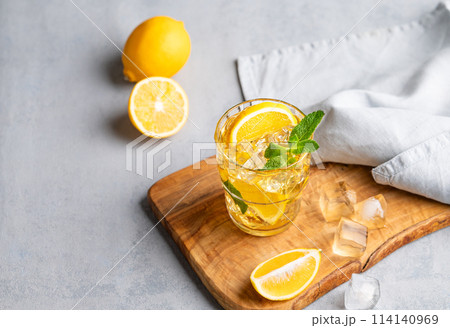 Iced drink with lemon, mint in a glass on a wooden board on a light background with citrus fruits. Iced drink with lemon, mint in a glass on a wooden board on a light background with citrus fruits. 114140969
