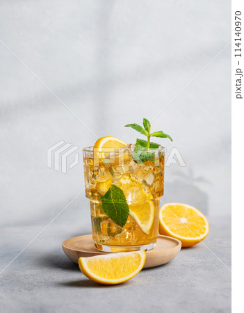 Iced drink with lemon, mint in a glass on a on a light background with shadow and citrus fruits. Iced drink with lemon, mint in a glass on a on a light background with shadow and citrus fruits. 114140970
