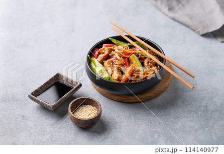 Stir-fry with soba noodles, meat and vegetables on a light background with chopsticks, soy sauce Stir-fry with soba noodles, meat and vegetables on a light background with chopsticks, soy sauce 114140977