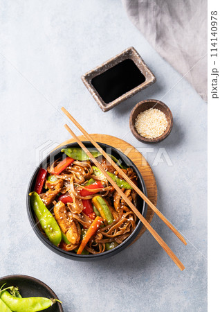 Stir-fry with soba noodles, meat and vegetables on a light background with chopsticks, soy sauce 114140978