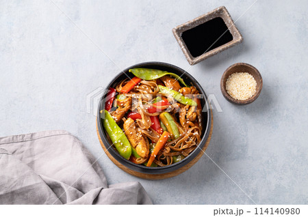 Stir-fry with soba noodles, meat and vegetables on a light background. Stir-fry with soba noodles, meat and vegetables on a light background. 114140980