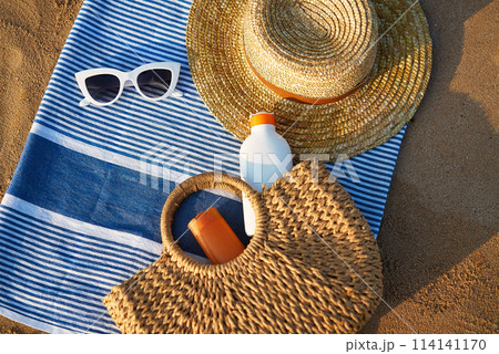 Sunbathing accessories on sandy beach, straw hat beside sunglasses, sunblock lotion in bag for skin protection, summer seaside holiday essentials on striped towel, outdoor UV care on sunny day. Sunbathing accessories on sandy beach, straw hat beside sunglasses, sunblock lotion in bag for skin protection, summer seaside holiday essentials on striped towel, outdoor UV care on sunny day. 114141170