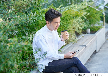コーヒーを飲みながらスマートフォンを操作する男性 114141368