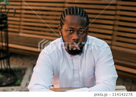 Close up portrait of a happy african american man smiling wearing ethnic dashiki clothes outdoor in summer cafe terrace background. Millennial generation student and youth. Close up portrait of a happy african american man smiling wearing ethnic dashiki clothes outdoor in summer cafe terrace background. Millennial generation student and youth. 114142278
