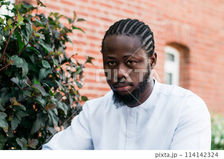 Portrait of a happy african american man wearing ethnic dashiki clothes outdoor in summer street wall. Millennial generation student and youth. Copy space Portrait of a happy african american man wearing ethnic dashiki clothes outdoor in summer street wall. Millennial generation student and youth. Copy space 114142324