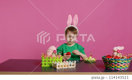 Smiling jolly preschooler painting eggs and ornaments for easter festivity preparations, using art and craft materials to decorate festive arrangements. Young boy having fun with tie dye. Camera B. 114143521