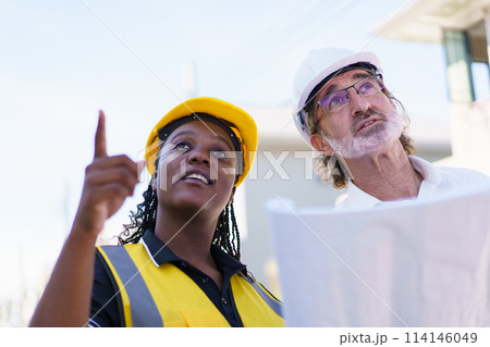 Team of engineer discuss at construction site. Female black ethnicity engineer taking to caucasian white client about the construction plan in blue print. Team of engineer discuss at construction site. Female black ethnicity engineer taking to caucasian white client about the construction plan in blue print. 114146049