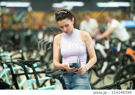 Focused woman reading product details on phone in bike shop Focused woman reading product details on phone in bike shop 114146599
