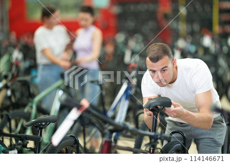 Interested cyclist selecting bike with comfortable saddle in store 114146671