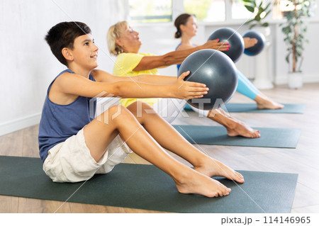 Family grandmother, mother and grandson perform fitness exercise sitting on floor with softball Family grandmother, mother and grandson perform fitness exercise sitting on floor with softball 114146965