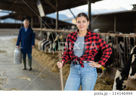 Portrait of positive woman farmer with pitchfork in cowhouse Portrait of positive woman farmer with pitchfork in cowhouse 114146994