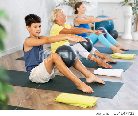 Preteen boy practicing fitness with softball between legs in light training room Preteen boy practicing fitness with softball between legs in light training room 114147723
