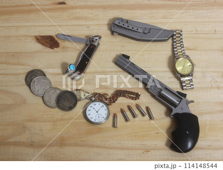 Gun With Silver Coins and Pocket Watch on Wooden Table 114148544