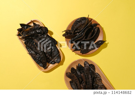 Different shape of wooden tray contains black locust fruits against on yellow background. High angle view with blank space for displaying product or adding text Different shape of wooden tray contains black locust fruits against on yellow background. High angle view with blank space for displaying product or adding text 114148682