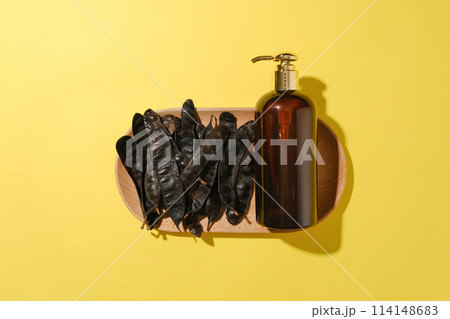 Top view at rectangle wooden tray with some black locust pods and a bottle without label displayed on. Empty space for advertising Top view at rectangle wooden tray with some black locust pods and a bottle without label displayed on. Empty space for advertising 114148683