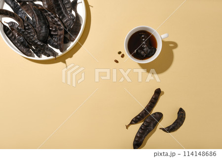 A round porcelain dish contains some locust fruit placed in top corner of photo, a cup of black liquid and some locust fruits lay flat on table. Top view photo with blank space for displaying A round porcelain dish contains some locust fruit placed in top corner of photo, a cup of black liquid and some locust fruits lay flat on table. Top view photo with blank space for displaying 114148686