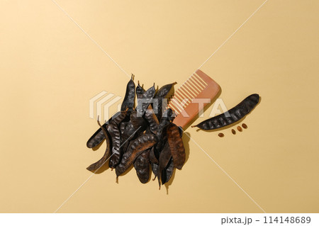 A wooden comb placed on light brown table surrounded by some black locust fruits with blank space for adding text or designing elements from high angle view 114148689
