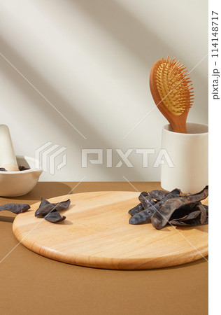 An empty wooden tray placed in center of brown table, a cup with wooden comb in, mortar and pestle, light gray background. Template for advertising product made from black locust pod An empty wooden tray placed in center of brown table, a cup with wooden comb in, mortar and pestle, light gray background. Template for advertising product made from black locust pod 114148717