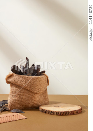 Front view locust template with a wooden empty tray beside a sackcloth bag of locust fruit and wooden comb placed on brown table. Blank space for displaying or presentation Front view locust template with a wooden empty tray beside a sackcloth bag of locust fruit and wooden comb placed on brown table. Blank space for displaying or presentation 114148720