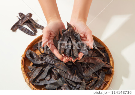 Beautiful female hand holding some black locust pods above a rattan tray full filled by black locust. View from above, close up, blank space Beautiful female hand holding some black locust pods above a rattan tray full filled by black locust. View from above, close up, blank space 114148736