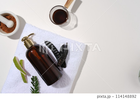 Unlabeled dark bottle flat lay on a blue towel, surrounded by organic ingredients for produce cosmetic manufacturing. Blank space for advertising, top view Unlabeled dark bottle flat lay on a blue towel, surrounded by organic ingredients for produce cosmetic manufacturing. Blank space for advertising, top view 114148892