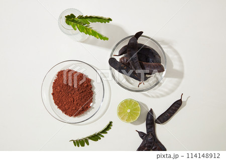 Glass dish of black locust pods placed by a glass bowl of locust powder, a half of lemon, fern. Top view photography with blank space for advertising Glass dish of black locust pods placed by a glass bowl of locust powder, a half of lemon, fern. Top view photography with blank space for advertising 114148912