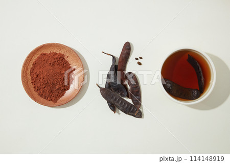 A wooden of black locust powder, some black locust pods, a bowl of locust soaked water placed side by side on white table. Photo with high angle shot, copy space A wooden of black locust powder, some black locust pods, a bowl of locust soaked water placed side by side on white table. Photo with high angle shot, copy space 114148919