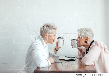 Two female senior collegues sitting next to each other in an cafe 114149089