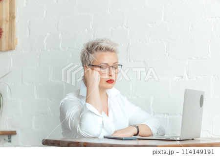 Smiling businesswoman is sitting at table with laptop and using think about business 114149191