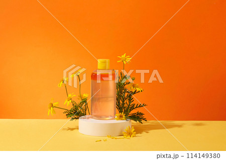 Mockup scene with a cosmetic bottle unlabeled displayed on white podium with fresh calendula flower on orange background . Minimal concept, front view. Space to add labels 114149380