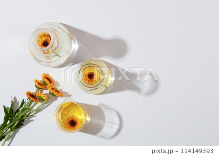 Mockup scene for cosmetic of calendula extract. Top view of fresh calendula flowers on lab glassware with essence decorated on a white background. Minimal concept, copy space Mockup scene for cosmetic of calendula extract. Top view of fresh calendula flowers on lab glassware with essence decorated on a white background. Minimal concept, copy space 114149393