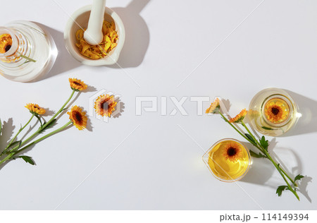 Fresh calendula flowers decorated with glass flask and small mortar and pestle on a white background. Concept for advertising cosmetics product extracted from calendula with space for presentation Fresh calendula flowers decorated with glass flask and small mortar and pestle on a white background. Concept for advertising cosmetics product extracted from calendula with space for presentation 114149394