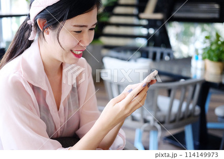 Beautiful Asian businesswoman is smiling and relaxing with smartphone in cafe and coffee shop Beautiful Asian businesswoman is smiling and relaxing with smartphone in cafe and coffee shop 114149973