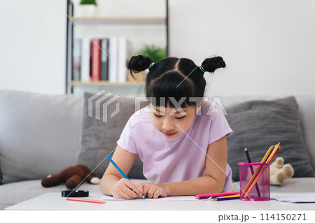 A young girl is sitting on a couch and drawing with crayons A young girl is sitting on a couch and drawing with crayons 114150271