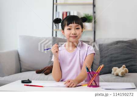 A young girl is sitting at a table with a pencil and a cup of crayons A young girl is sitting at a table with a pencil and a cup of crayons 114150272