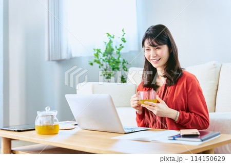 休日に自宅のリビングで学び直しやリスキリングの勉強の為にノートパソコンでオンライン講座を受講する女性 114150629