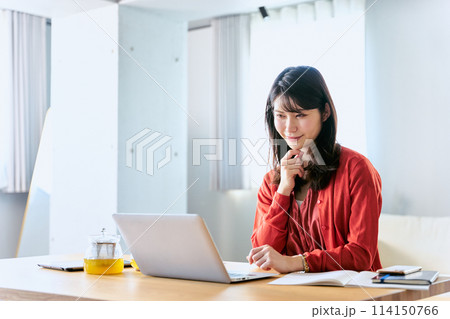 自宅のリビングにノートパソコンを広げて真剣な表情で仕事をする30代の1人の女性 自宅のリビングにノートパソコンを広げて真剣な表情で仕事をする30代の1人の女性 114150766